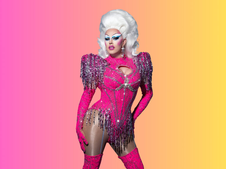 Dragqueen met witte haren in een kleurrijke roze en gele outfit straalt tijdens Drag Camp in Amsterdam.